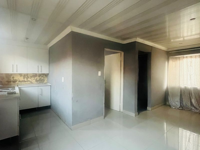 Open-plan living area featuring tiled floors, recessed lighting, and a compact kitchen corner with built-in cabinetry.