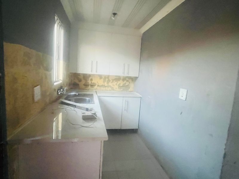 A compact kitchen area featuring basic built-in cabinetry and a sink, currently requiring wall finishing and backsplash installation to complete the space.