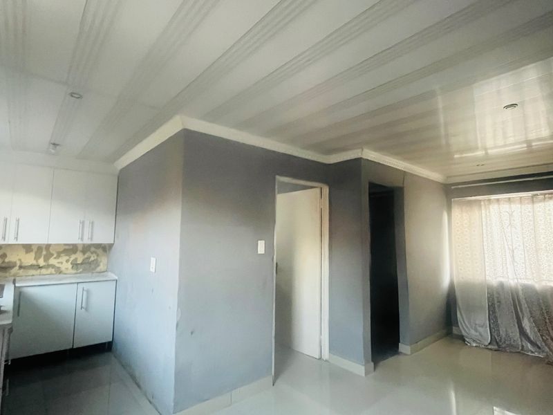An open-plan living and kitchen area featuring tiled floors, built-in cabinetry, and a coved ceiling, currently in need of finishing touches.