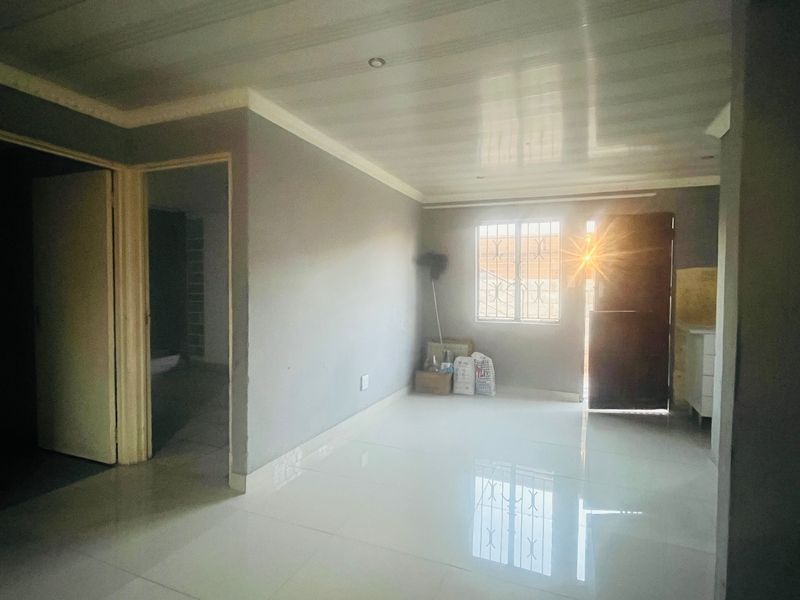 An empty living room featuring tiled flooring, a panelled ceiling, and security bars on the window, offering a blank canvas for interior design.
