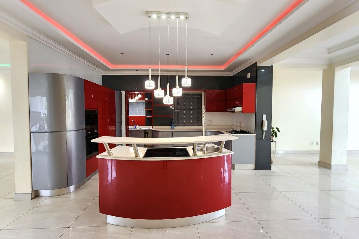 Modern open-plan kitchen featuring a distinctive curved island, high-gloss cabinetry, built-in appliances, and ambient cove lighting throughout the space.