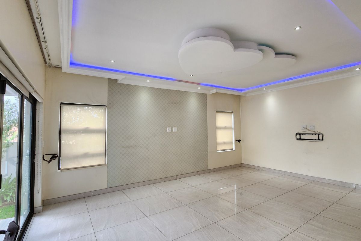 Spacious living area featuring modern recessed ceiling lighting, large format floor tiles, and a textured feature wall with access to the garden.