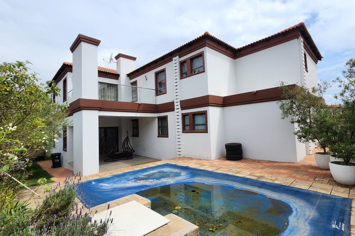 Rear view of a two-story house featuring a swimming pool with a cover, a covered patio area, and an upper-level balcony with glass balustrades.