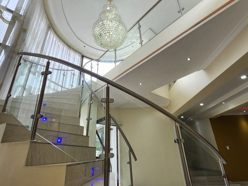 Grand entrance hall featuring a striking curved staircase with glass balustrades, elegant tiled flooring, and a sophisticated crystal chandelier.