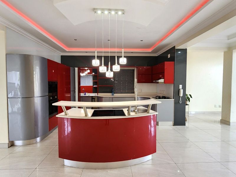 Modern open-plan kitchen featuring a distinctive curved island, high-gloss cabinetry, built-in appliances, and ambient cove lighting throughout the space.