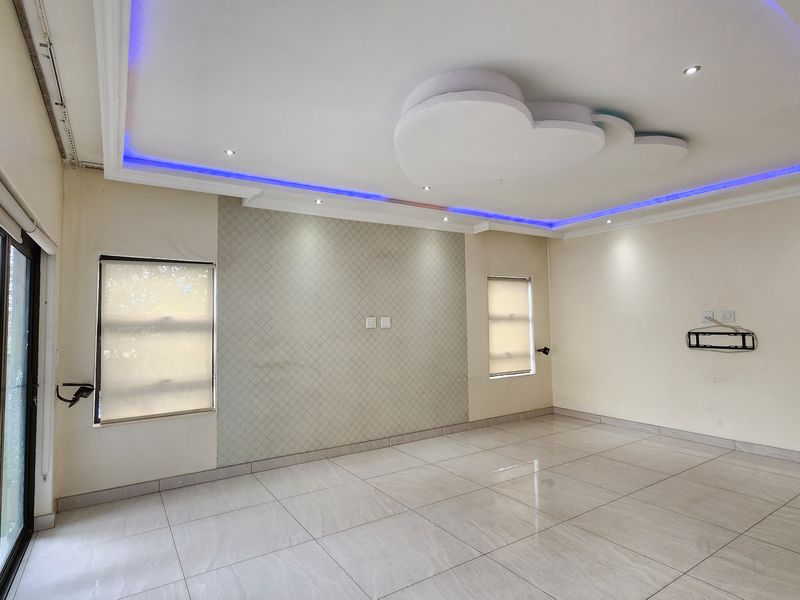 Spacious living area featuring modern recessed ceiling lighting, large format floor tiles, and a textured feature wall with access to the garden.