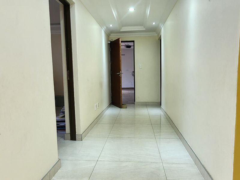 A bright, clean hallway featuring neutral tiled flooring, recessed ceiling lighting, and coved detailing, providing a seamless transition between rooms.
