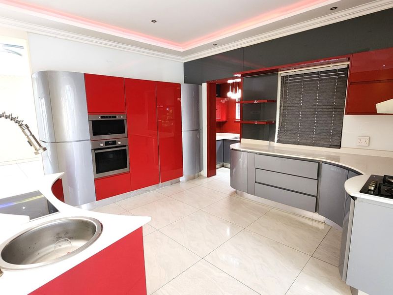 Modern kitchen featuring high-gloss red and grey cabinetry, built-in appliances, gas hob, and sleek tiled flooring with integrated ambient ceiling lighting.