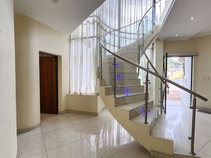 Spacious entrance hall featuring a striking curved staircase with glass balustrades, stainless steel handrails, and integrated LED stair lighting.