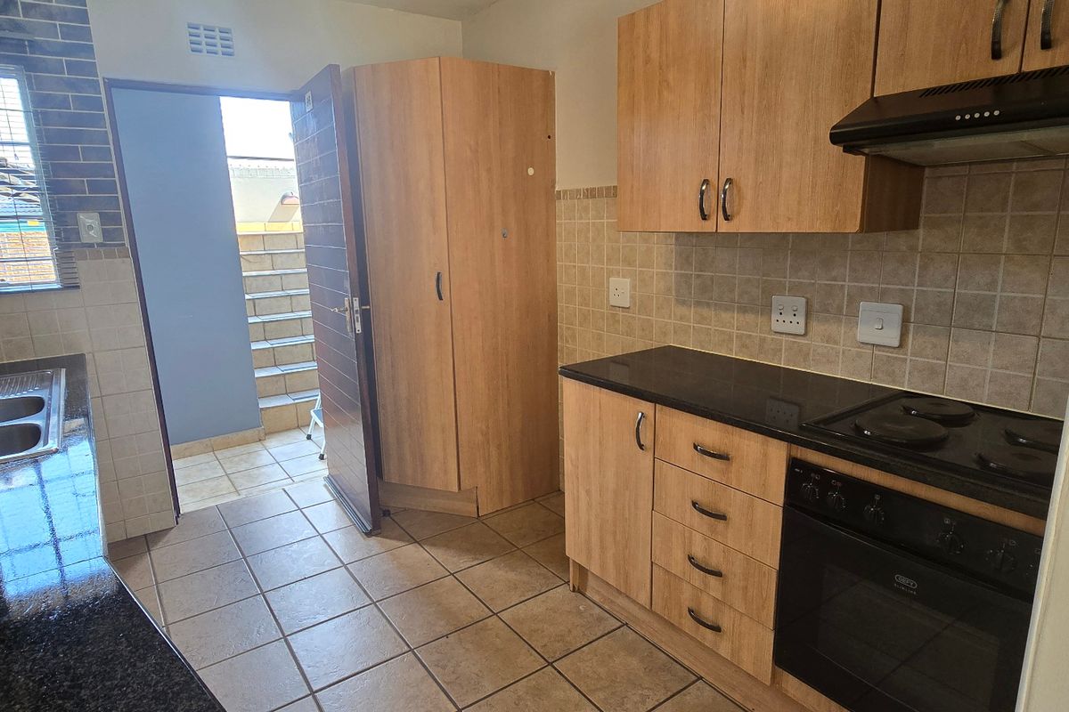 Functional kitchen featuring built-in wooden cabinetry, black granite countertops, integrated oven and stove, and tiled backsplash with direct access to an outdoor area.