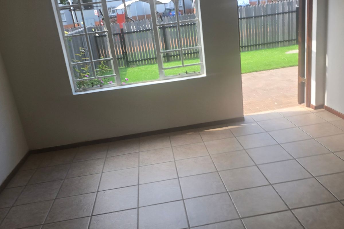 An empty living room featuring neutral tiled flooring and a large window, with direct access to an outdoor patio area.