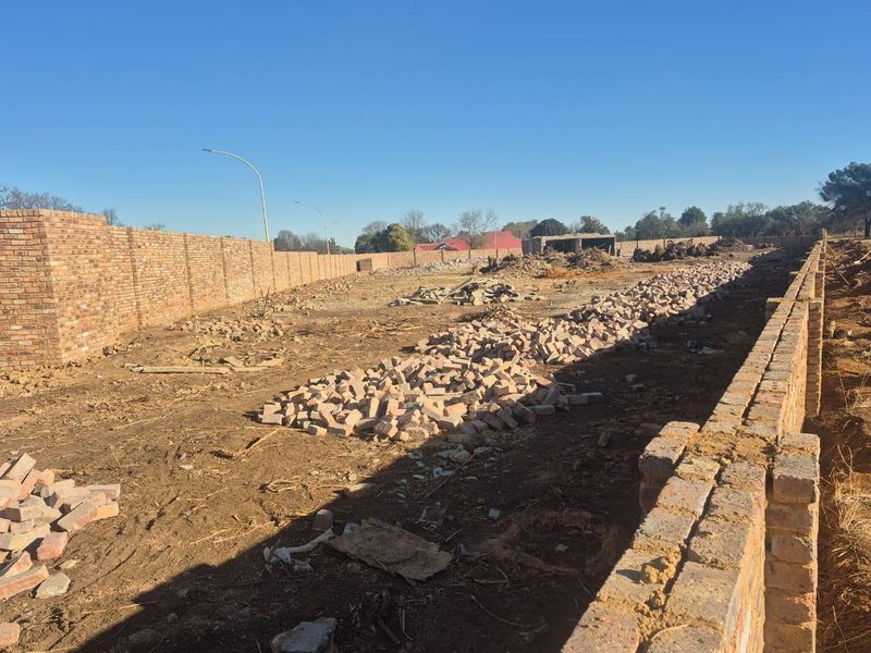 A large, undeveloped commercial plot enclosed by perimeter brick walls, currently featuring construction debris and uneven ground.