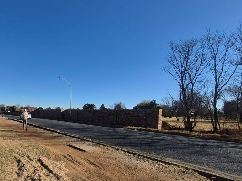 Street view showing the asphalt road frontage and the brick boundary wall of the commercial property.