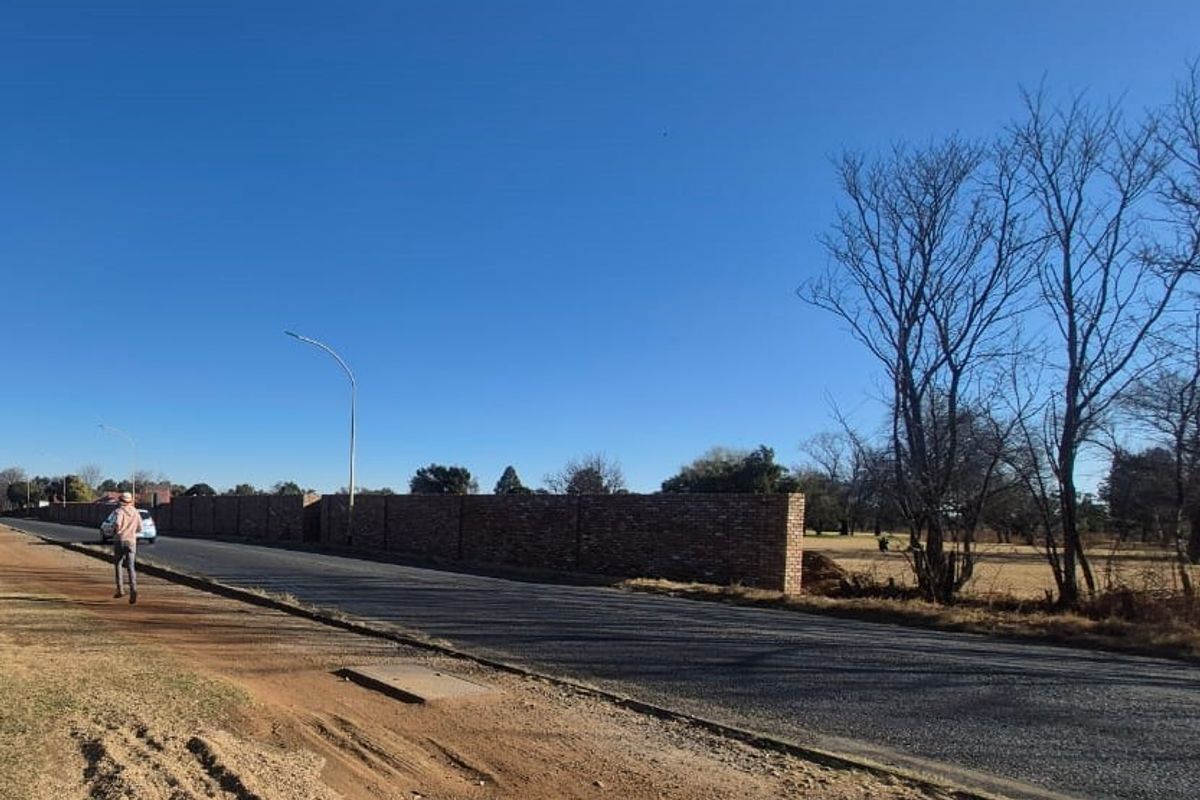 Street view showing the asphalt road frontage and the brick boundary wall of the commercial property.