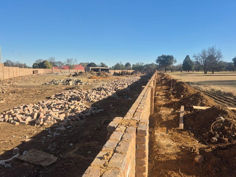A large commercial plot under development featuring a newly constructed perimeter brick wall and significant site clearing and earthworks in progress.