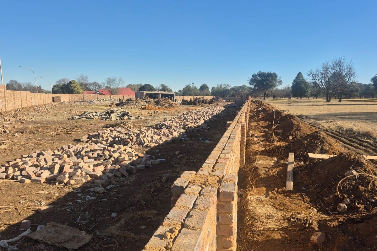 A large commercial plot under development featuring a newly constructed perimeter brick wall and significant site clearing and earthworks in progress.