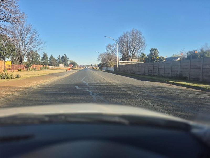 A view of the street approach leading to the property, featuring an asphalt road and concrete boundary walling.