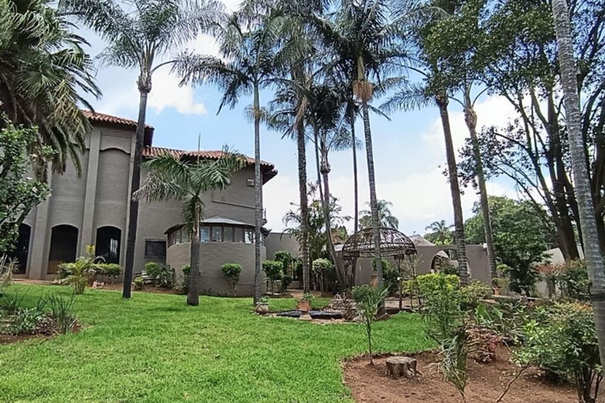 A spacious rear garden featuring mature palm trees, a well-maintained lawn, and a decorative wrought iron gazebo set against the property's stucco exterior.