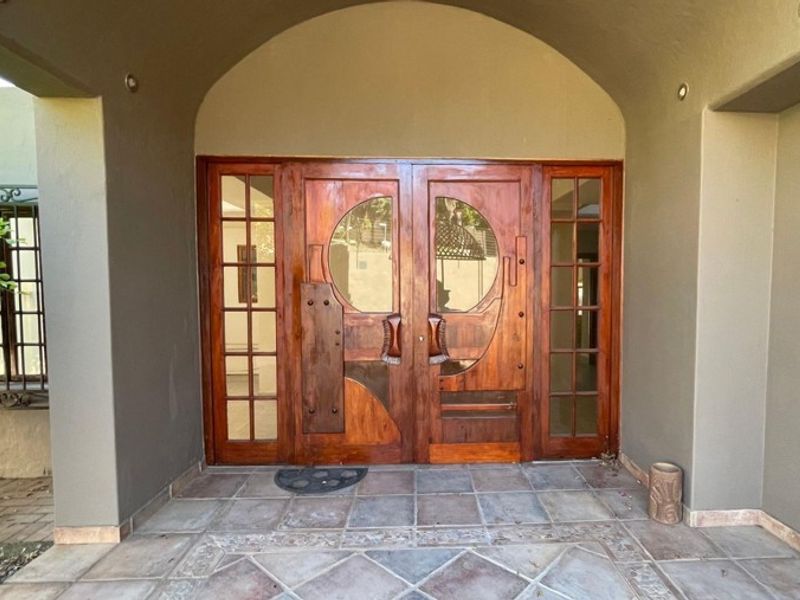 Covered entrance porch featuring a distinctive double wooden front door with glass inserts and tiled flooring.