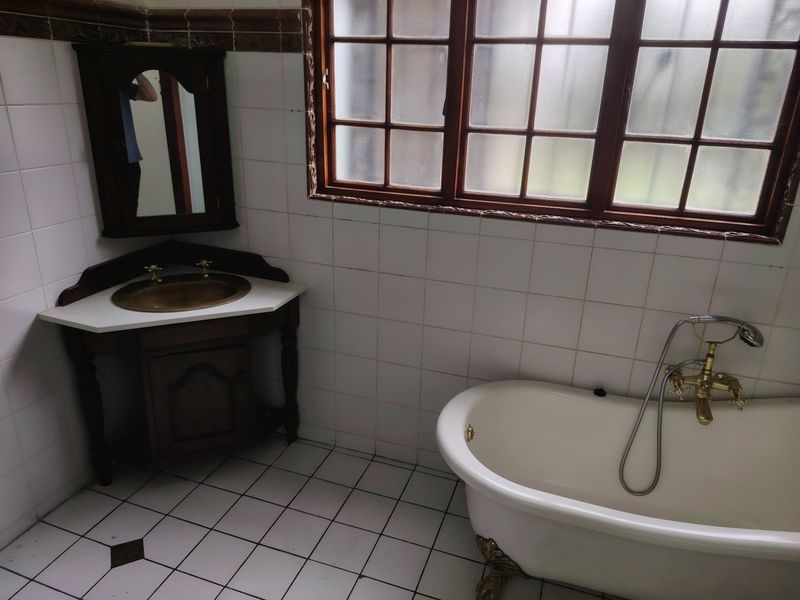 A vintage-style bathroom featuring a classic clawfoot bathtub, a corner vanity unit with a brass basin, and traditional wall and floor tiling.
