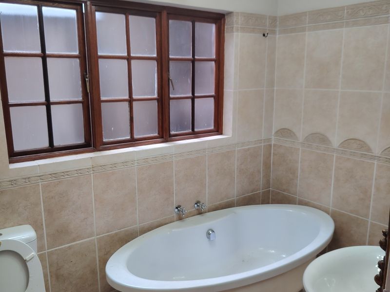 A traditional bathroom featuring a freestanding bathtub, ceramic tiling, and a timber-framed window, offering a classic aesthetic with potential for modern updates.