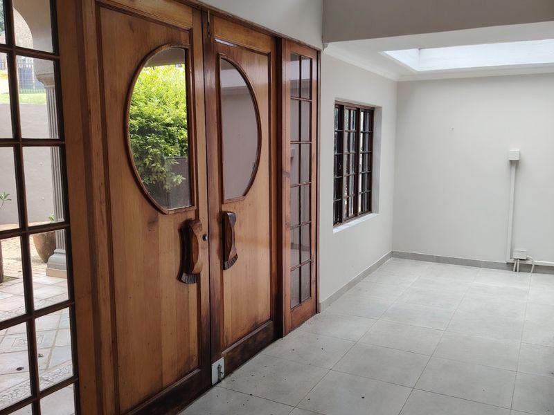 A bright entrance hall featuring timber-framed glass doors, tiled flooring, and a recessed ceiling with a clerestory window for natural light.