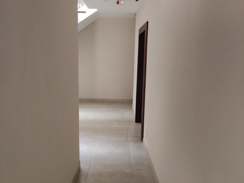 A bright, empty hallway featuring neutral tiled flooring, a decorative crystal chandelier, and a skylight providing natural illumination.