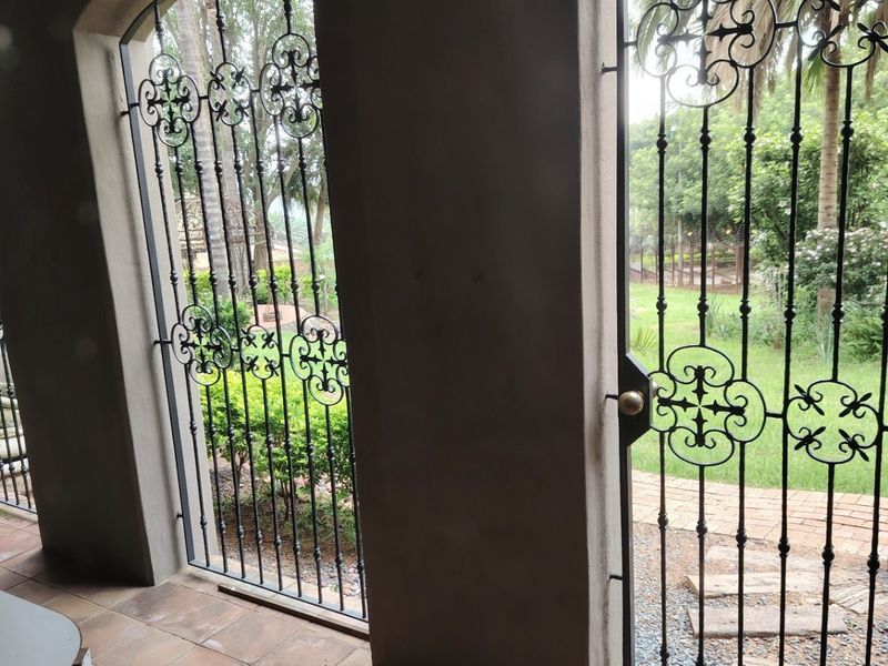 A covered patio area featuring arched doorways with decorative wrought iron security gates and tiled flooring, overlooking a garden.