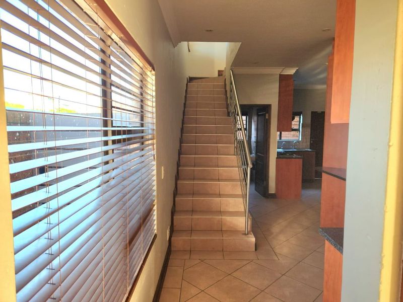A bright hallway featuring a tiled staircase with a stainless steel balustrade, leading towards the kitchen area.