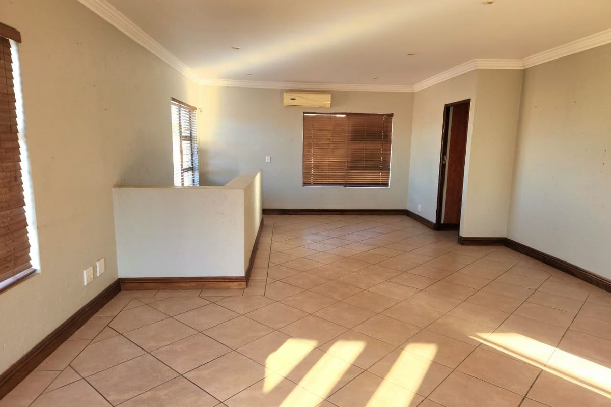 Spacious, light-filled living area featuring neutral tiled flooring, recessed downlighting, and a wall-mounted air conditioning unit.