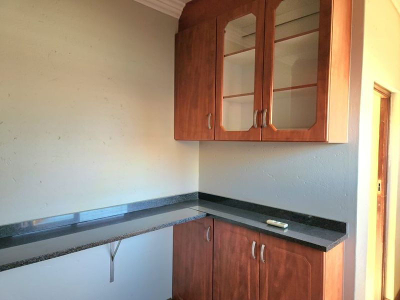 A functional scullery or utility area featuring wood-finish cabinetry, granite countertops, and glass-fronted upper storage units.