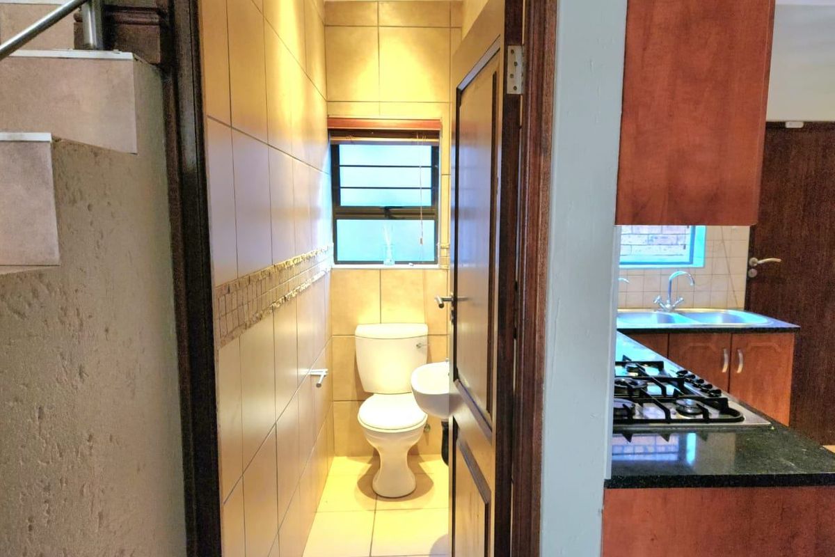 A compact guest bathroom featuring tiled walls, a wall-mounted basin, and a standard toilet, conveniently located adjacent to the kitchen area.