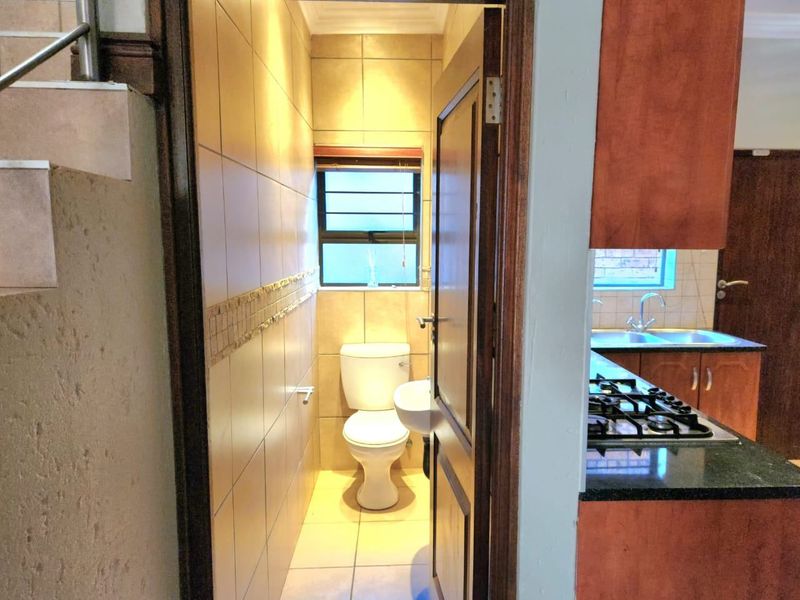 A compact guest bathroom featuring tiled walls, a wall-mounted basin, and a standard toilet, conveniently located adjacent to the kitchen area.