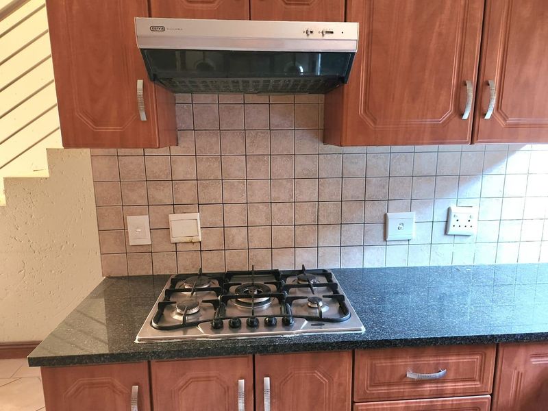 Kitchen area featuring a gas hob, stainless steel extractor fan, granite countertops, and tiled backsplash with wooden cabinetry.