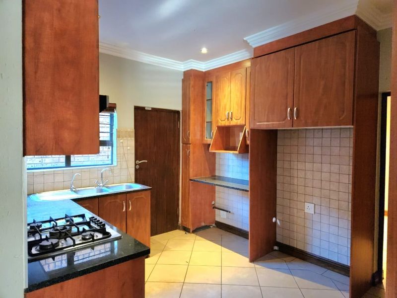 A functional kitchen featuring wooden cabinetry, granite countertops, a gas hob, and tiled splashbacks, offering a practical layout for culinary activities.