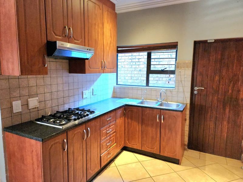 A functional kitchen featuring wooden cabinetry, a gas hob with extractor fan, double sink, and tiled flooring.