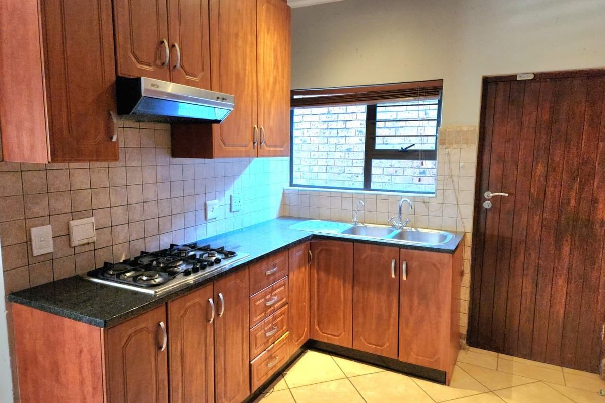 A functional kitchen featuring wooden cabinetry, a gas hob with extractor fan, double sink, and tiled flooring.