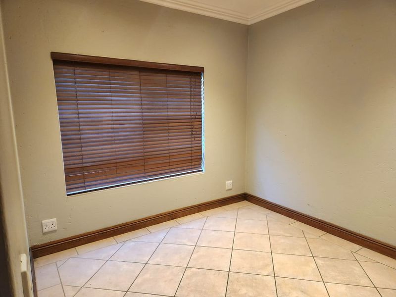 An empty bedroom featuring neutral tiled flooring, wooden venetian blinds, and simple wall finishes, providing a clean canvas for personalization.