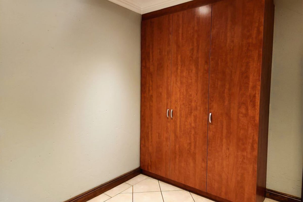 A clean, empty bedroom featuring neutral walls, tiled flooring, and a large, well-maintained built-in wooden wardrobe.