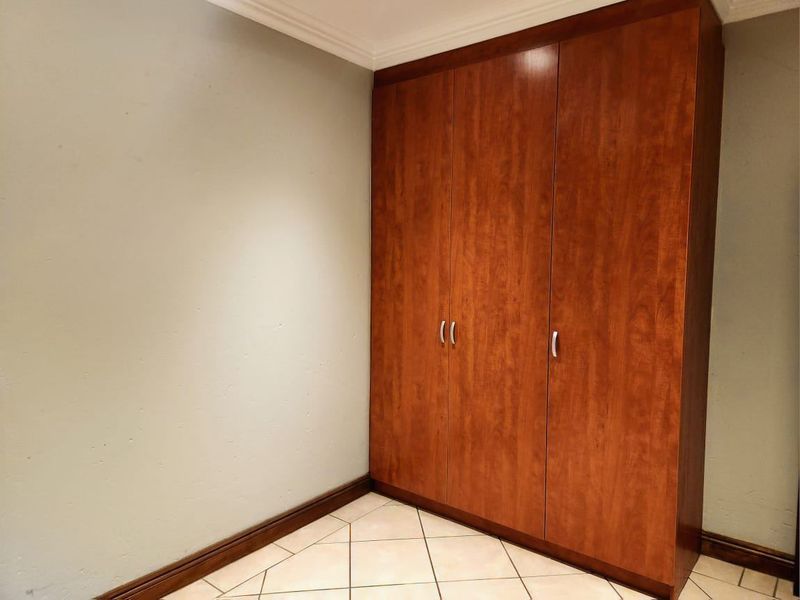 A clean, empty bedroom featuring neutral walls, tiled flooring, and a large, well-maintained built-in wooden wardrobe.
