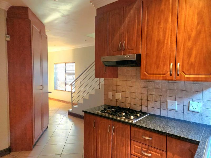 A functional kitchen featuring wooden cabinetry, granite countertops, a gas hob with extractor fan, and tiled backsplash, leading to an open staircase area.