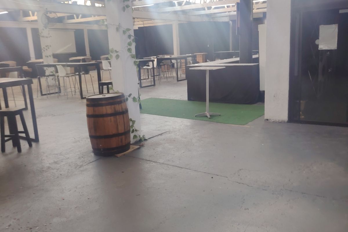 Spacious open-plan commercial area featuring exposed industrial roof trusses, concrete flooring, and natural light streaming through overhead skylights.