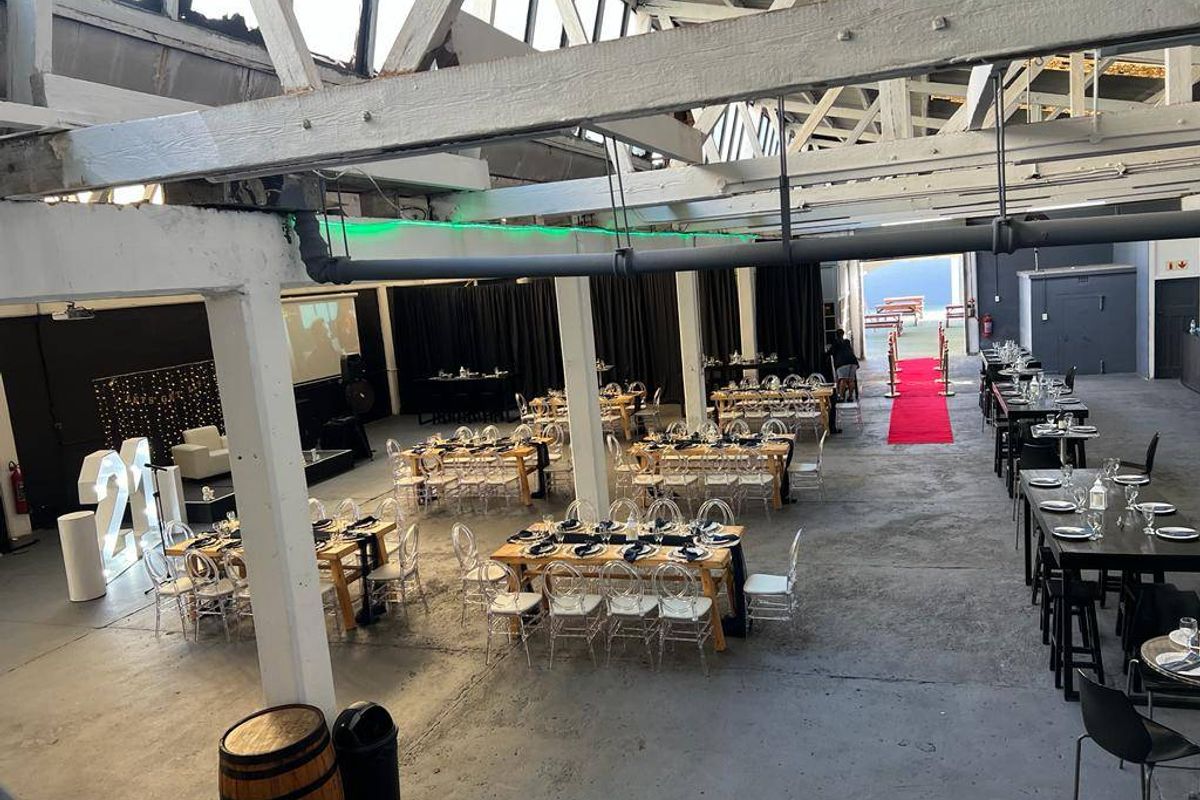Spacious industrial-style commercial event venue featuring high vaulted ceilings with exposed trusses, concrete flooring, and an open-plan layout suitable for large gatherings.