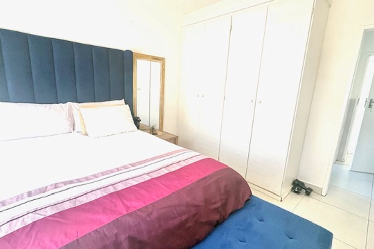 A well-lit bedroom featuring built-in cupboards and neutral tiled flooring, providing a clean and functional living space.