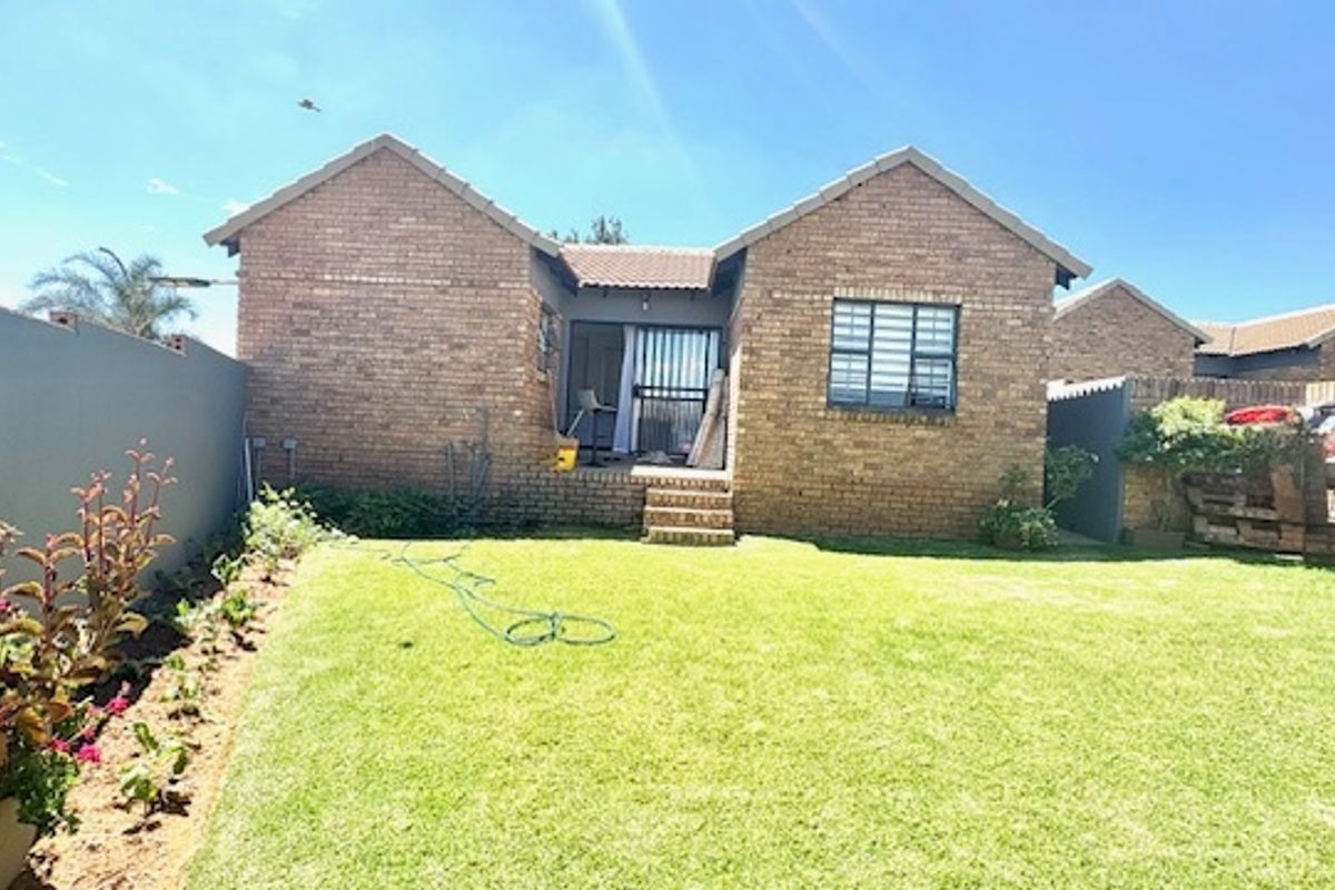 Rear view of a face brick cluster home featuring a private garden, lawn, and secure sliding door access.