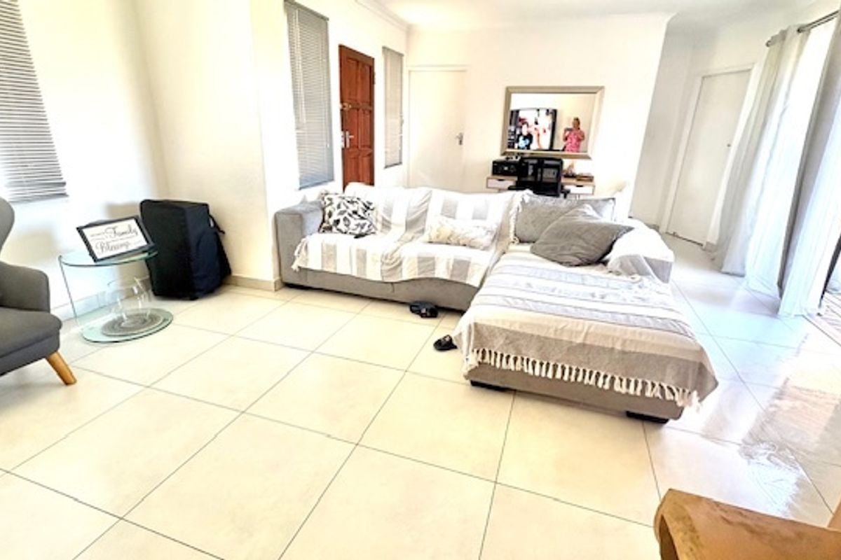 A bright, open-plan living area featuring large format floor tiles, neutral walls, and direct access to an outdoor patio through sliding glass doors.