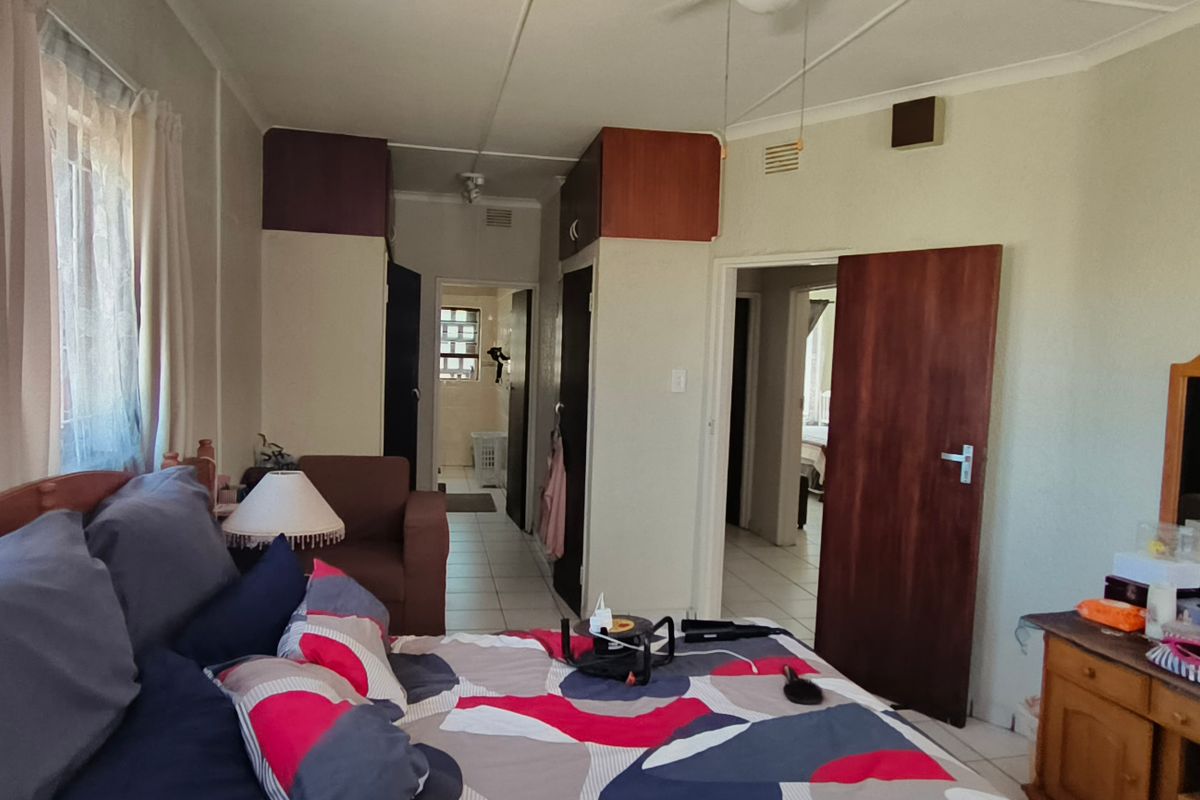 A bedroom featuring built-in cupboards, tiled flooring, and a ceiling fan, with direct access to an adjoining room and hallway.