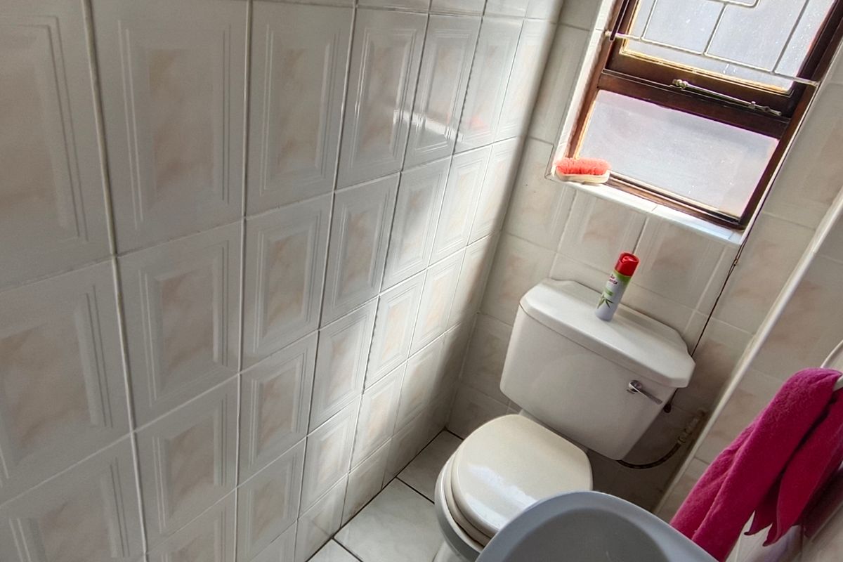 A functional bathroom featuring ceramic wall and floor tiling, a standard toilet, and a towel ring, with a window providing natural light.