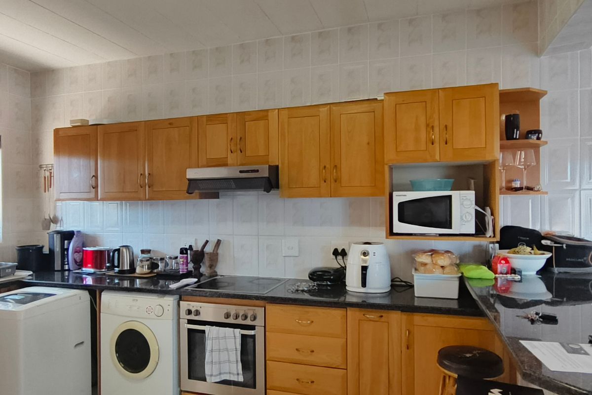 A functional kitchen featuring wooden cabinetry, granite countertops, a built-in oven with hob, and a breakfast bar, providing ample workspace and storage.