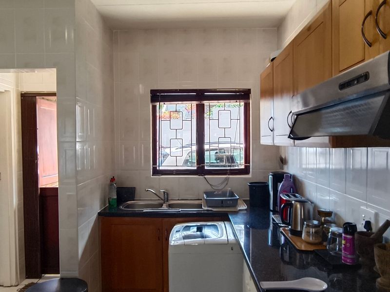 A functional kitchen featuring wooden cabinetry, granite countertops, a tiled splashback, and an integrated extractor fan, with an adjacent utility area.